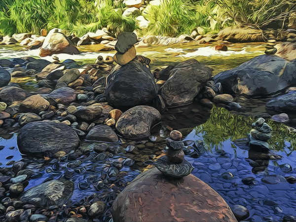A stream reflecting the blue sky with lots of rocks, a few have been made into cairns
